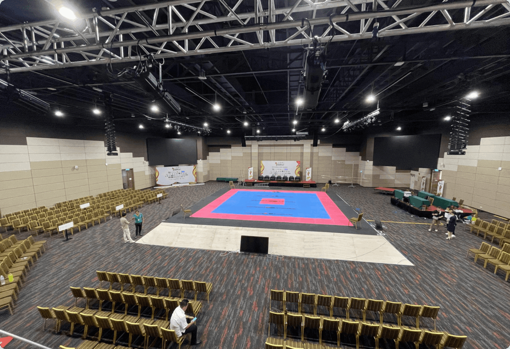 Spacious indoor venue with central blue-pink mat and empty chairs, calm and anticipatory mood.