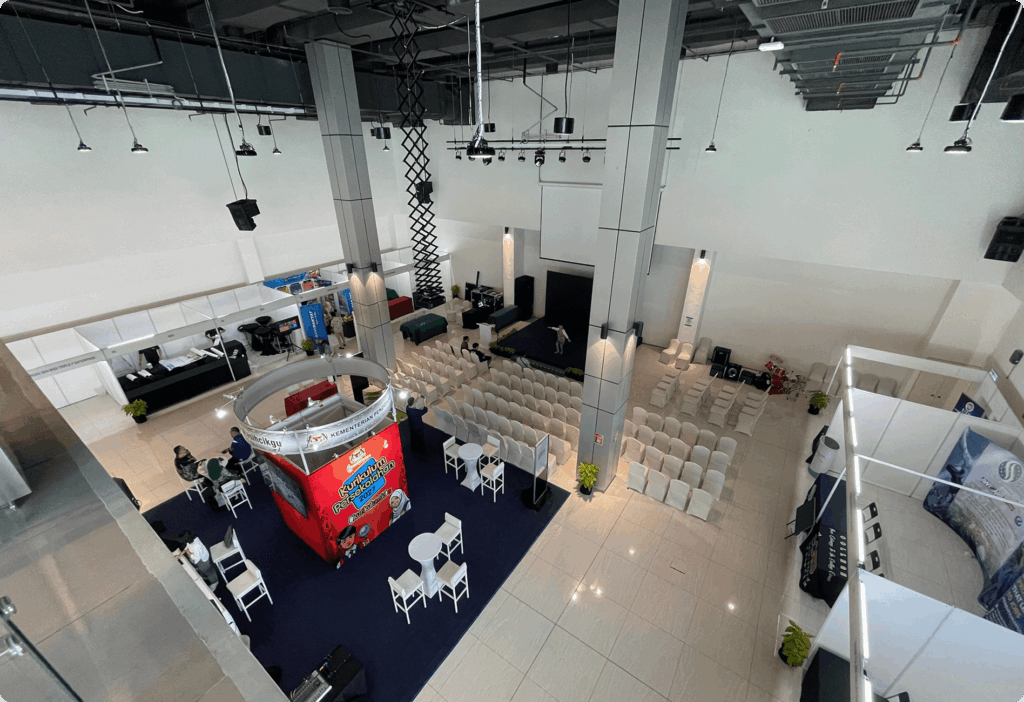 Spacious event hall with white seating, red booth on blue carpet, and modern lighting, conveying professionalism.